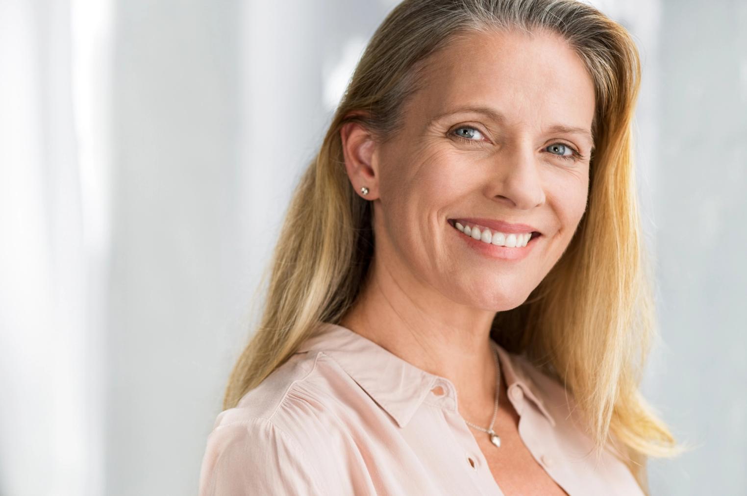 A blonde woman with blue eyes smiles directly at the viewer.