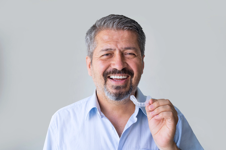 A smiling man holding a clear dental appliance