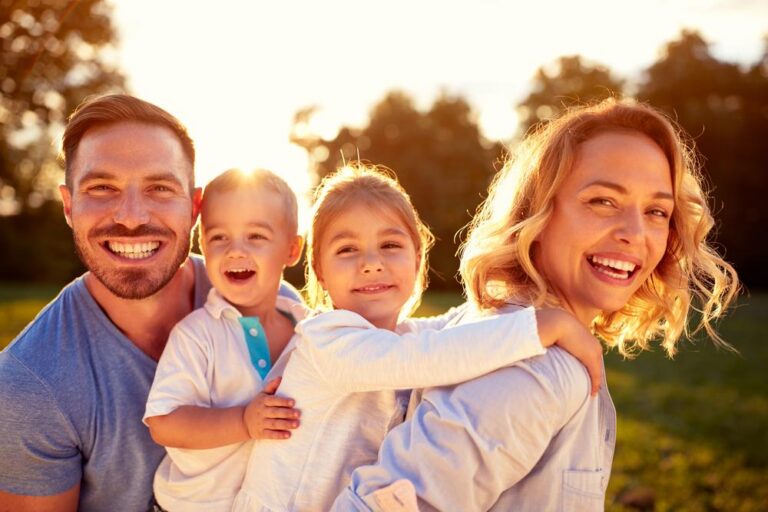A smiling family of four outdoors in warm sunlight.