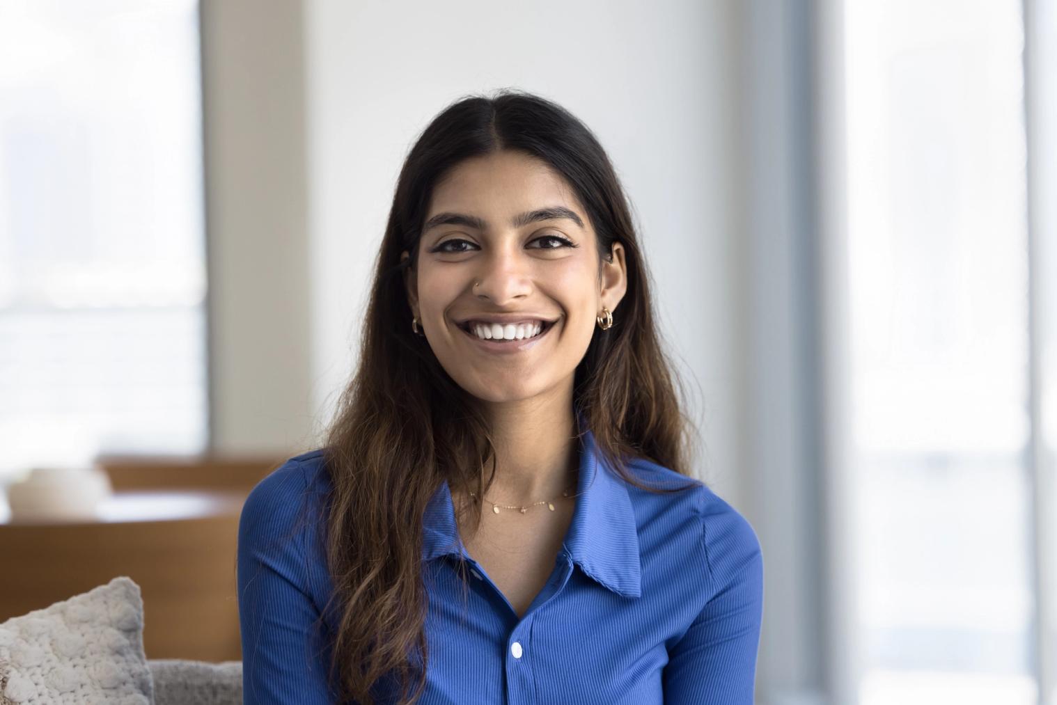 A smiling young woman with long dark hair wearing a blue shirt.