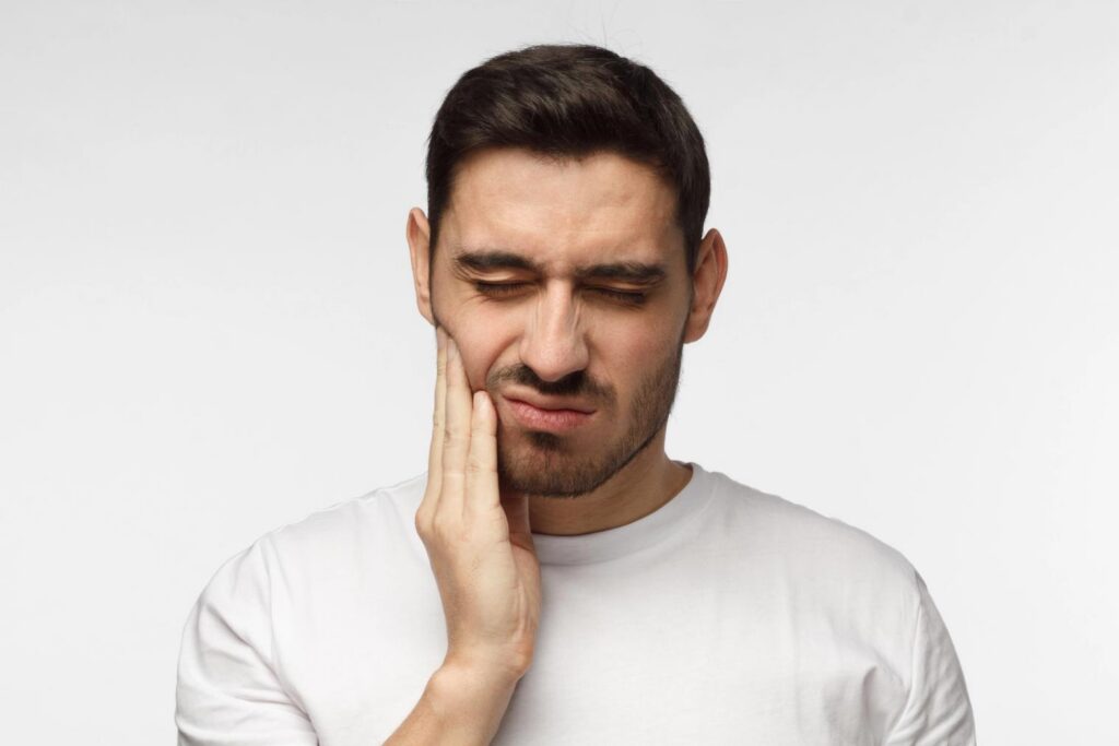 Man grimacing with closed eyes, holding his jaw in pain.