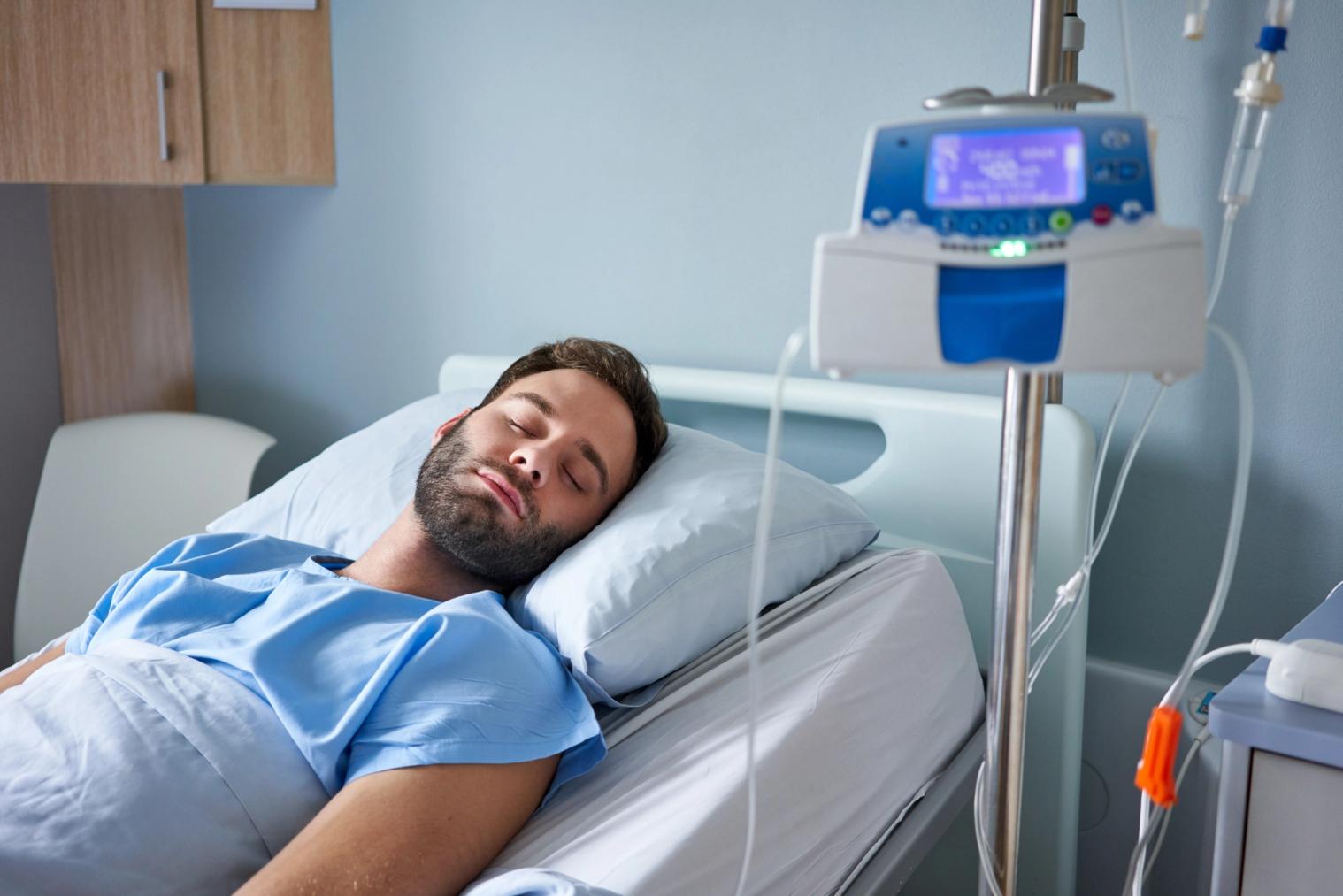 Man sleeping in a hospital bed with an IV drip.