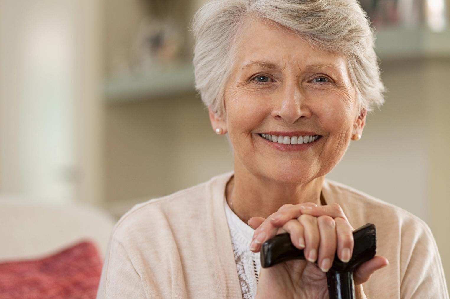 Smiling senior woman with short gray hair holding a cane.