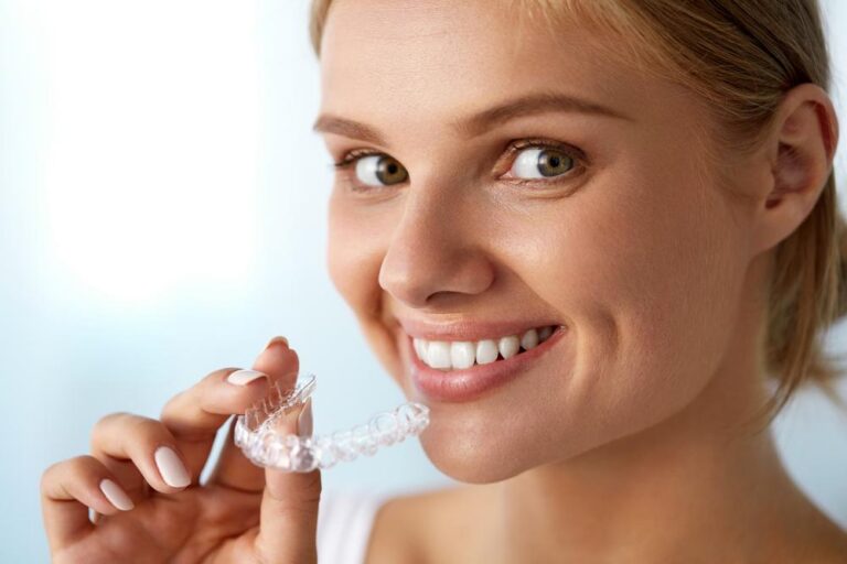 Smiling woman holding clear dental aligners.