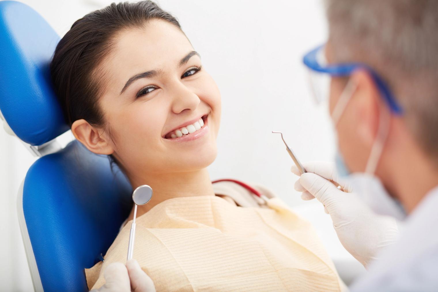 Smiling woman in dental chair with dentist holding tools.