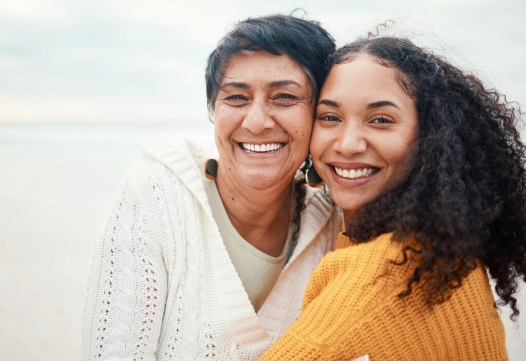 Two smiling women embracing on a beach.